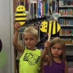 Kids smile and hold up paper bee craft